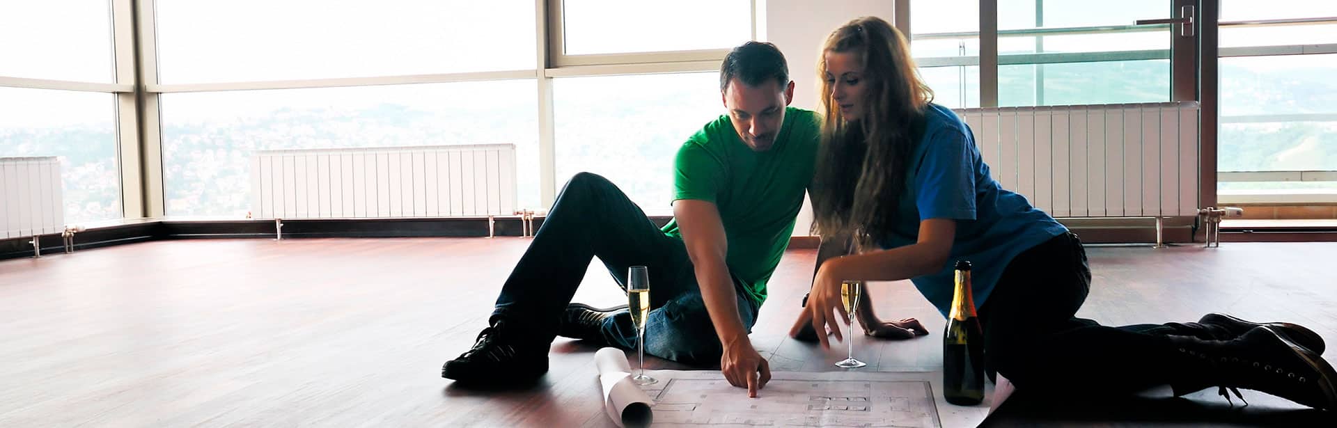 Couple sitting on the floor, looking at a floor plan blueprint.