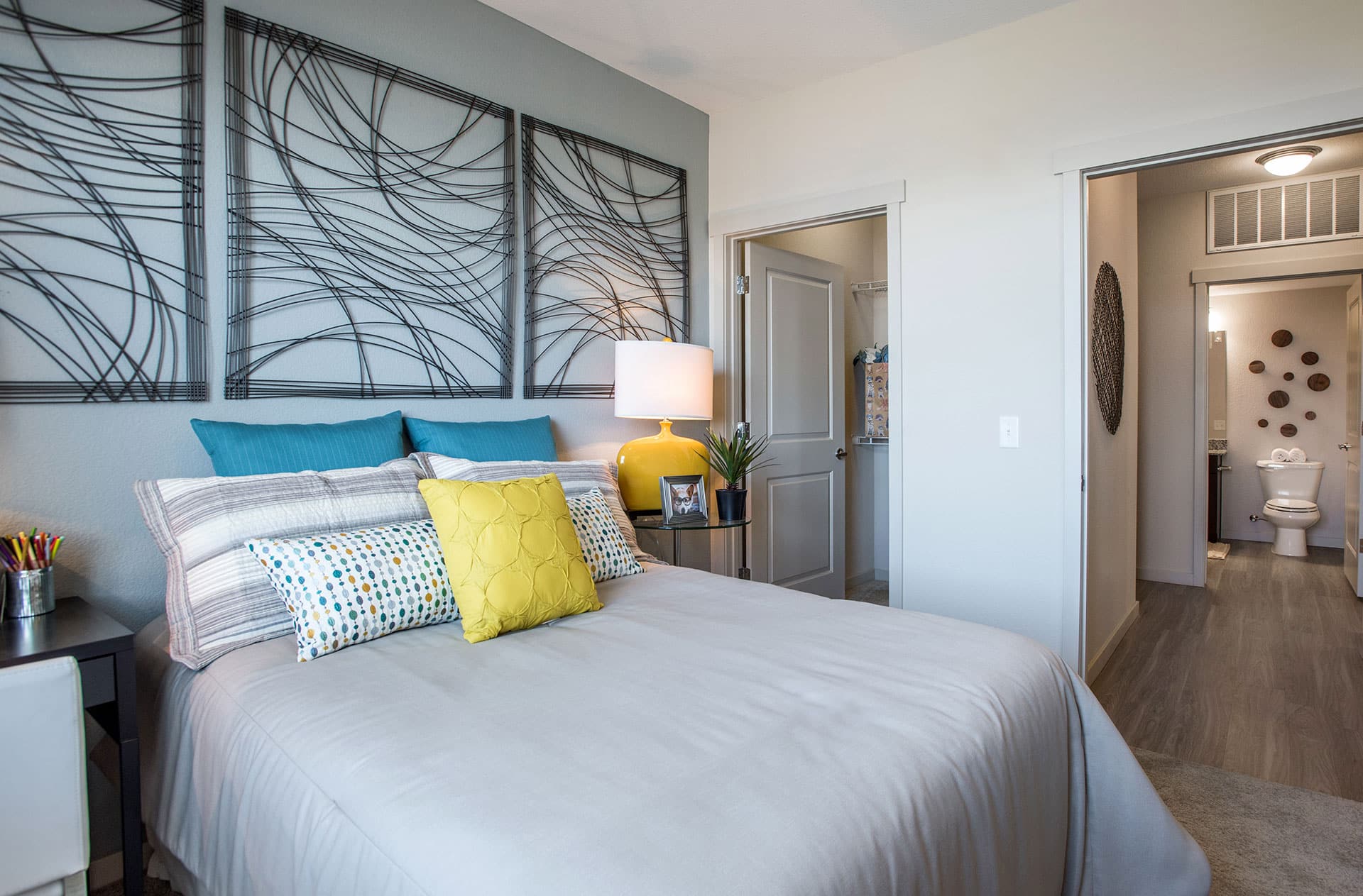 Bedroom with gray bedding, teal and yellow accent pillows.