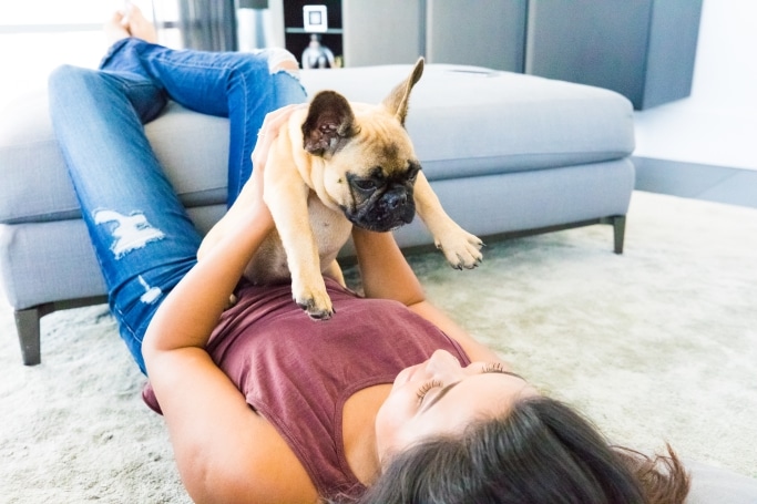 Girl laying on floor holding a small tan and black boxer puppy