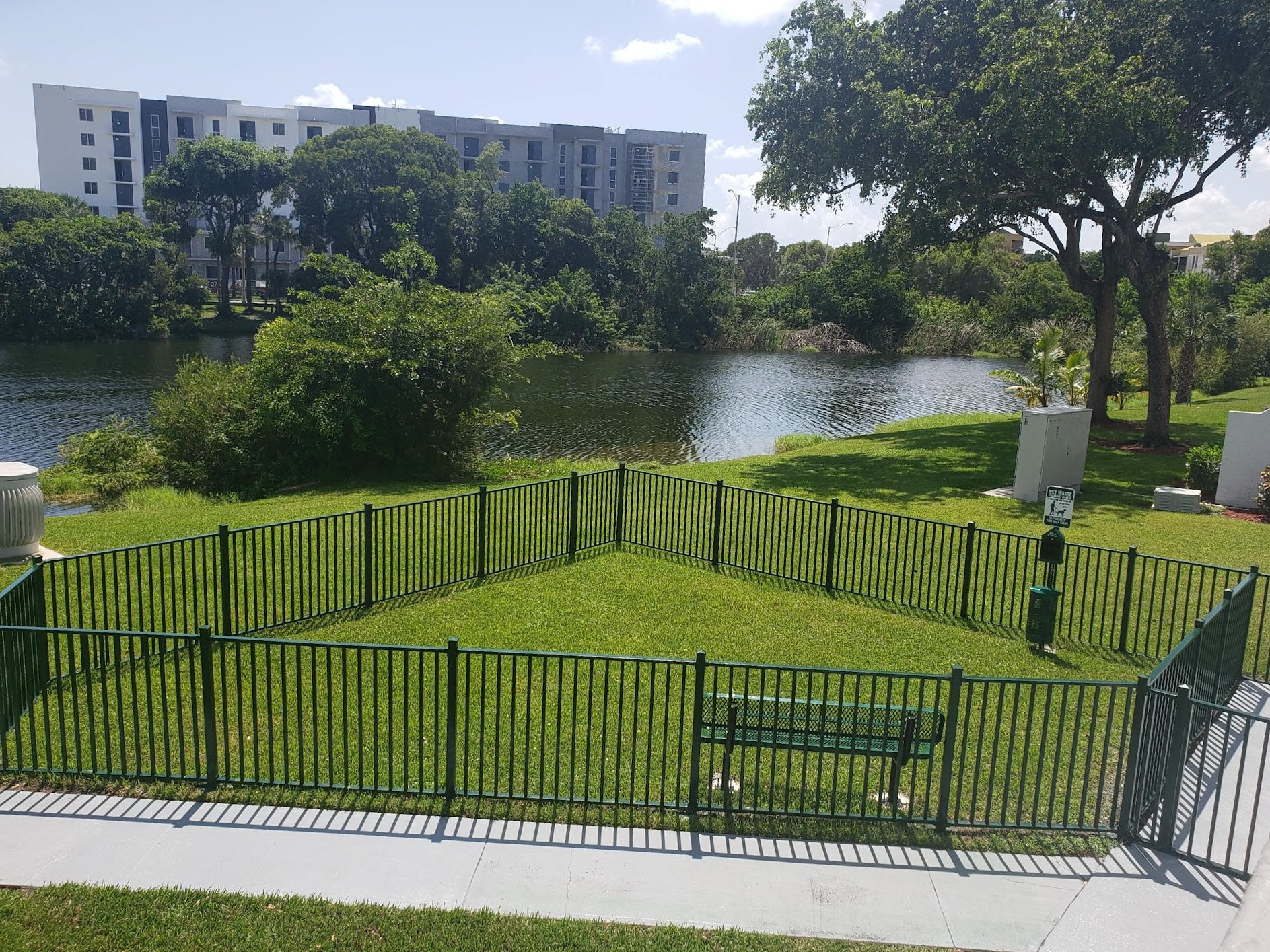 Fenced dog park area with green grass and bench for sitting