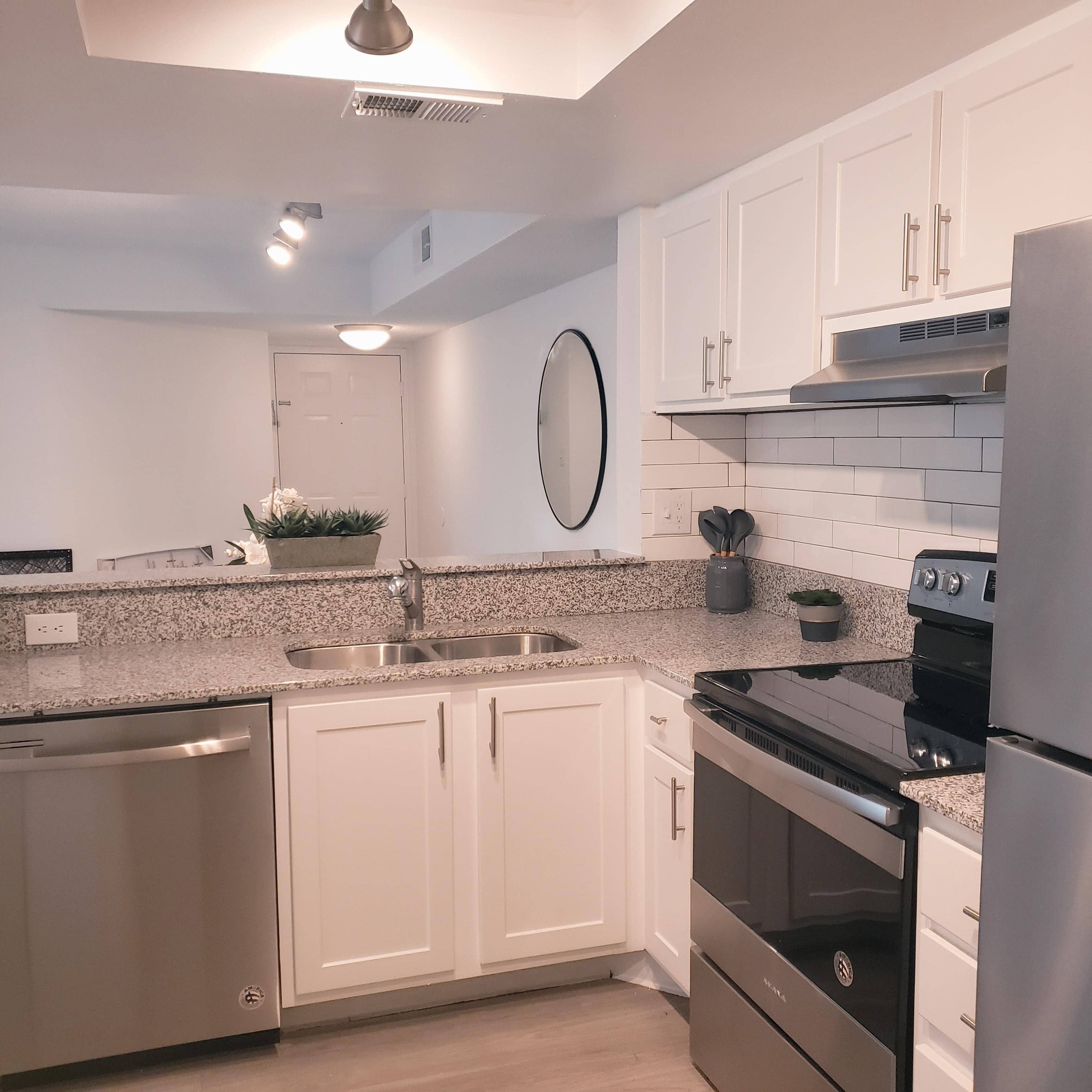 Cascades Model kitchen with white cabinets, stainless steel appliances, white tile backsplash and round mirror.