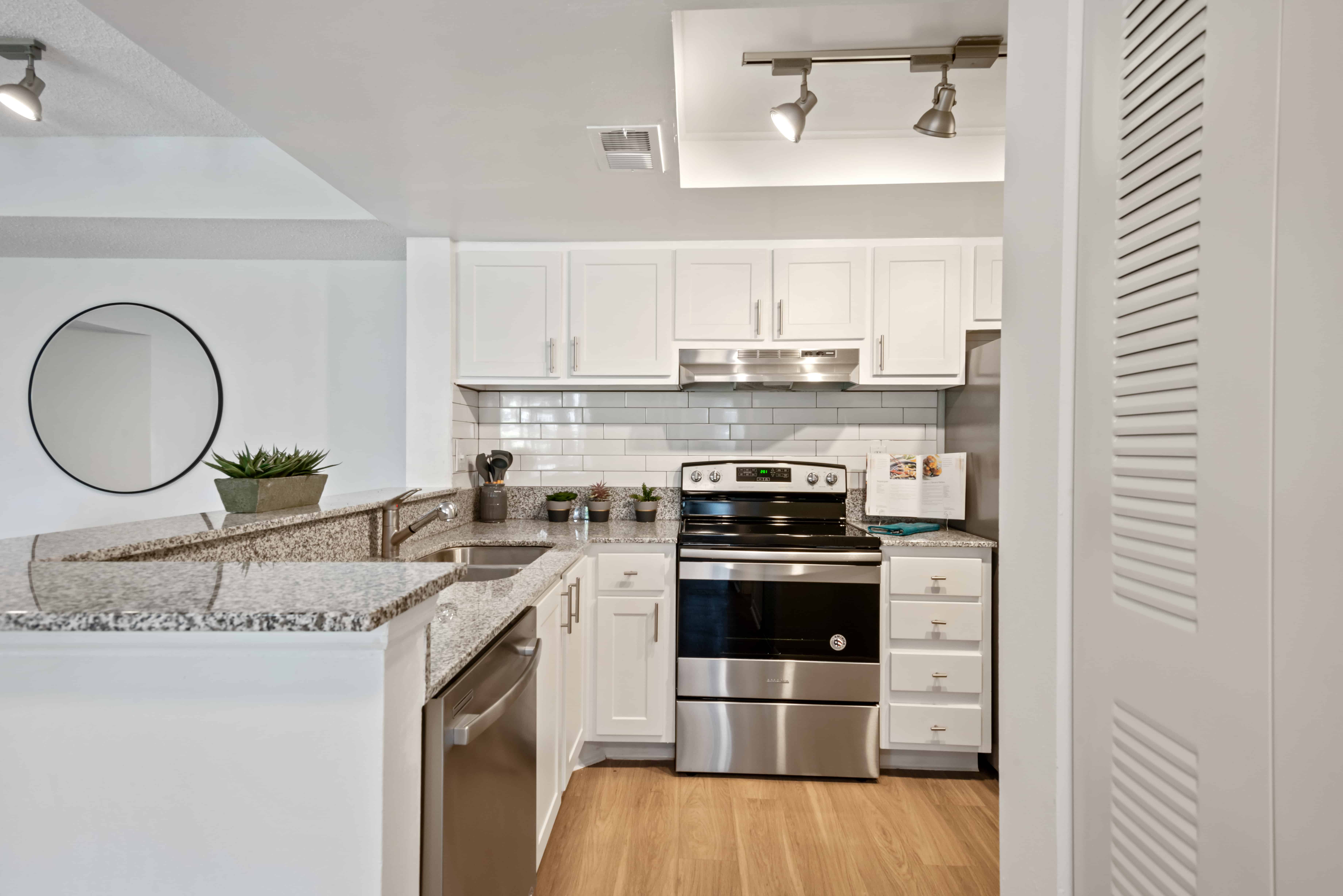 Open kitchen with stainless appliances , white cabinets and grey and black speckled granite countertop