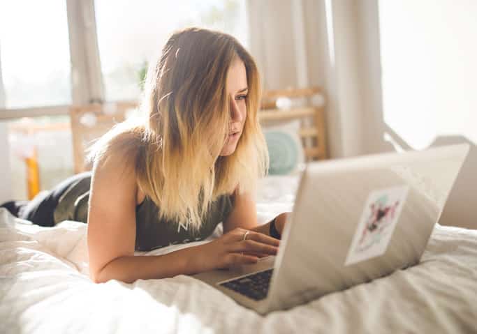 Young woman sitting on bed looking at a laptop.